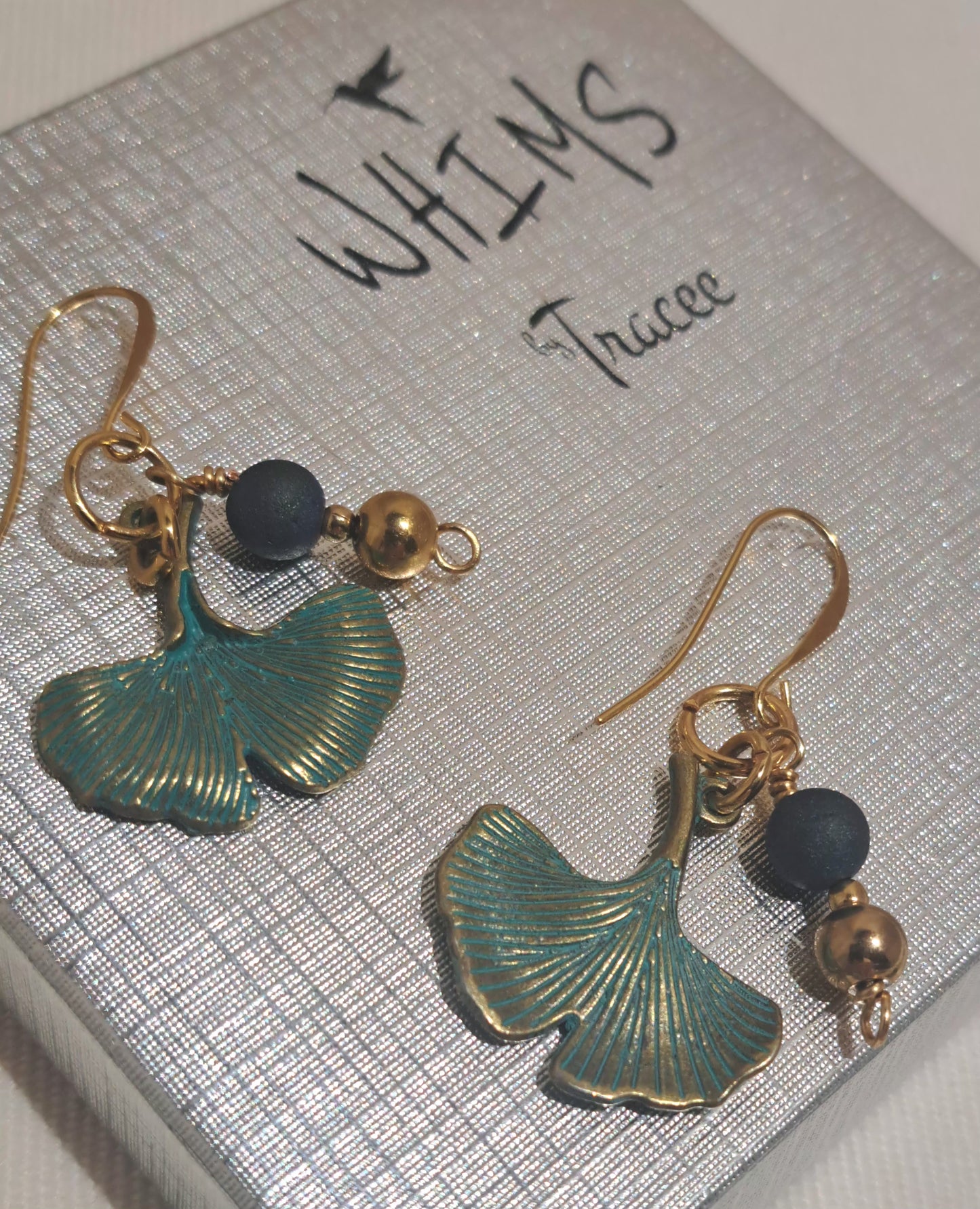 Close up of Ginko Charm earrings with blue druzy accent beads on gold shepherds hook ear wires