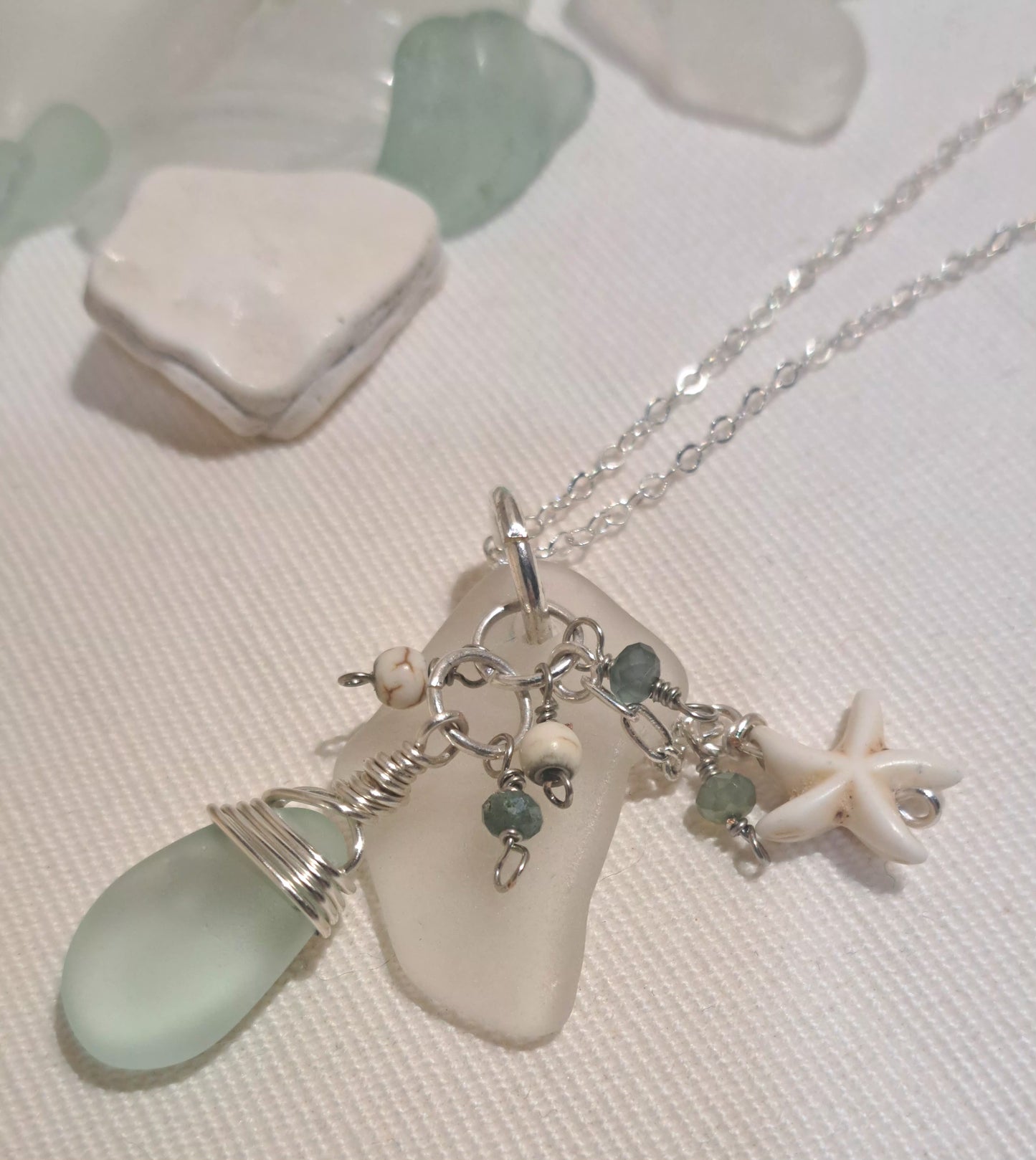 Clear sea glass chip hung on silver chain with pale green wire wrapped tear drop shaped glass and ivory star charm
