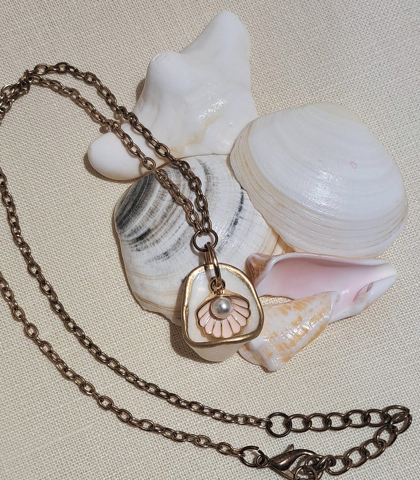 Cup shaped sea shell pendant with pink clam shell charm and hanging pearl.