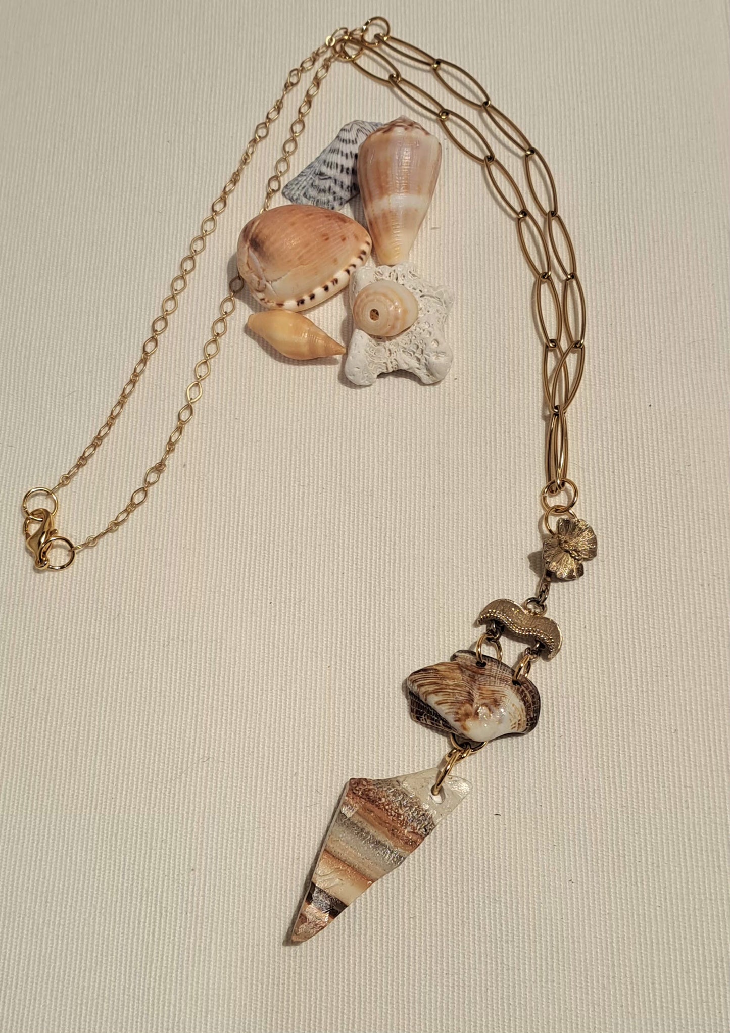 Gold paperclip style chain necklace with focal Caymanite stone in a triangular shape and a polished sea shell hung from a vintage textured gold clasp