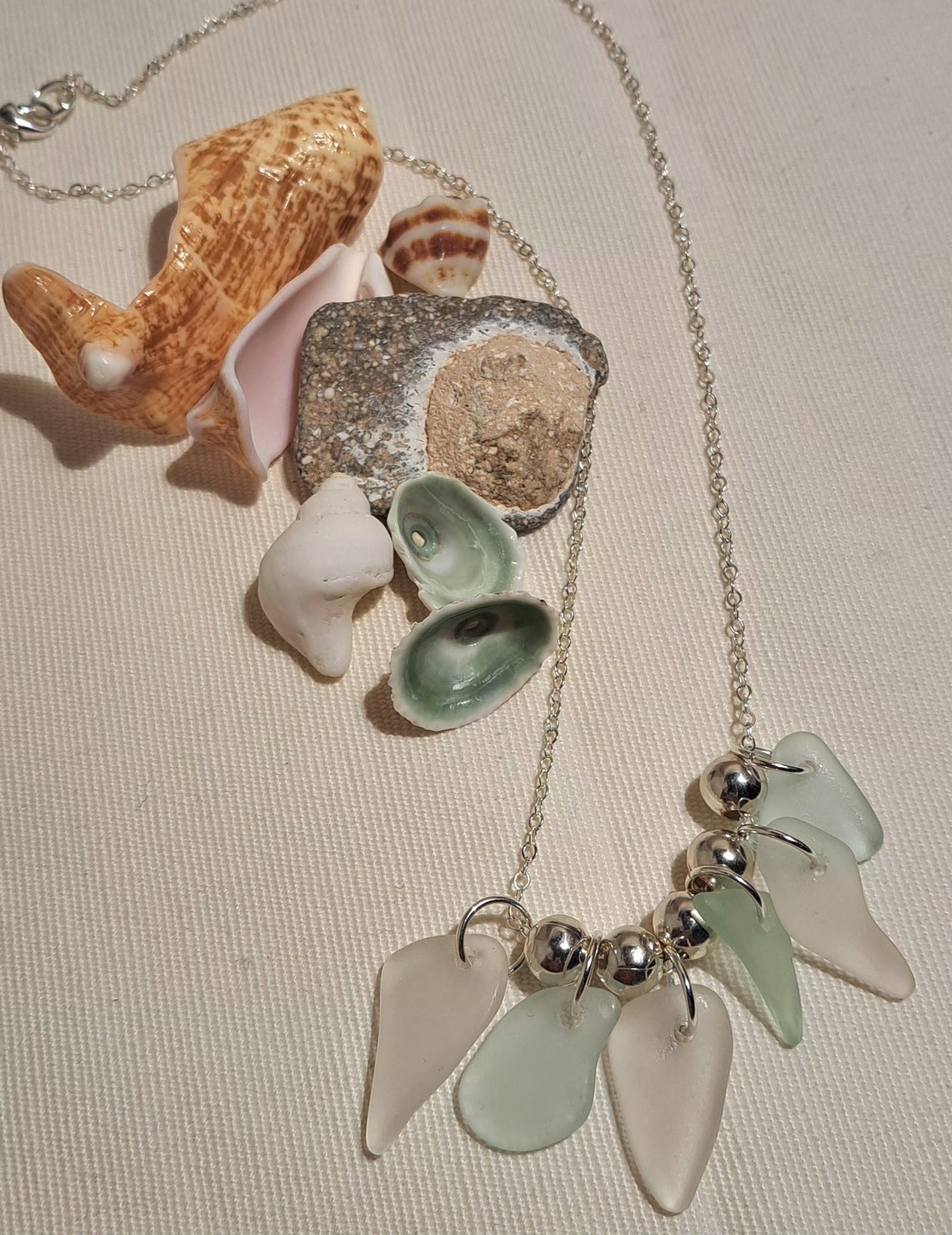 Pale white and pale greenish blue sea glass chips strung together on a silver chain with silver bead spacers between the sea glass