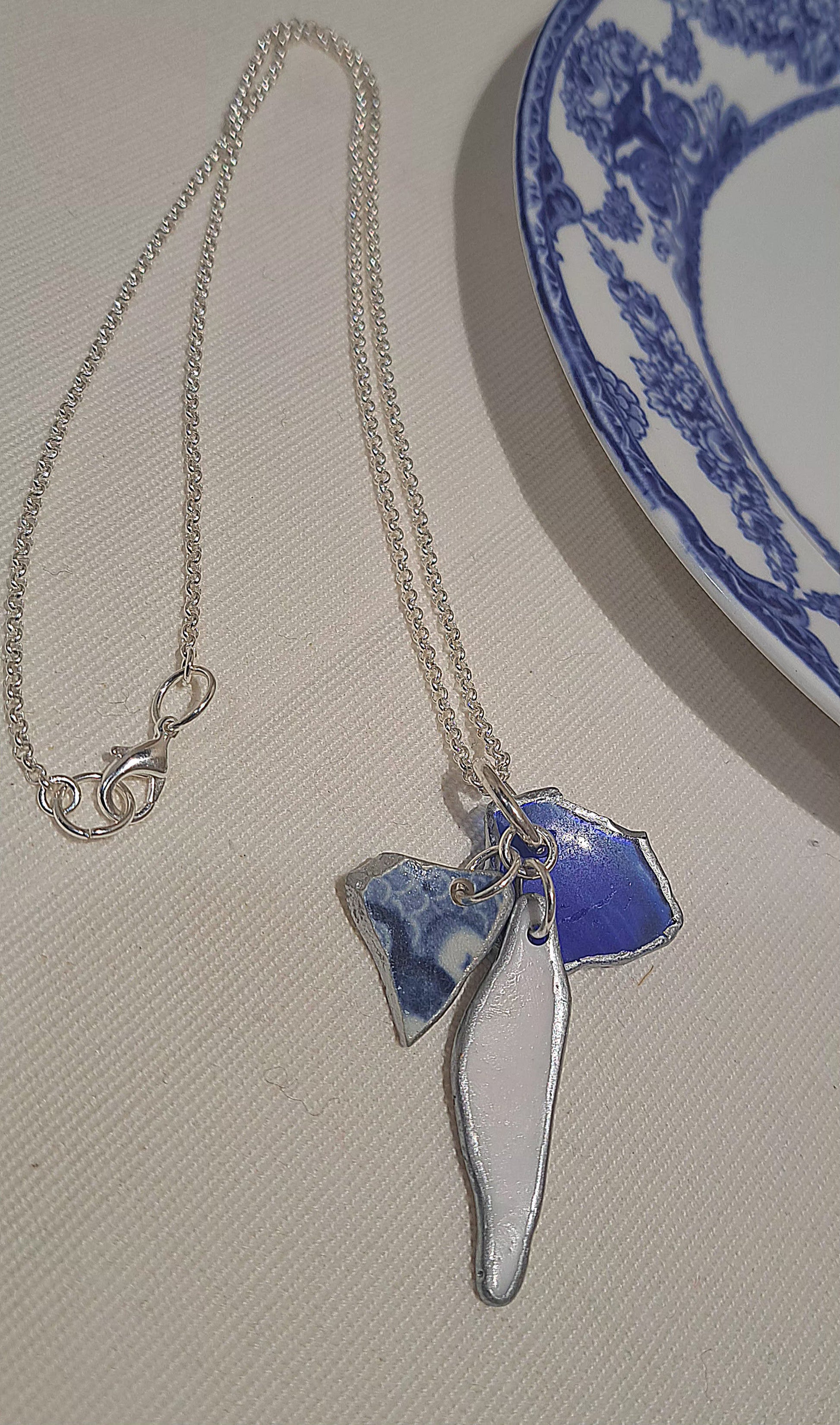 Silver chain necklace with a white shell elongated chip, a deep blue sea glass chip with silver edging and a flow blue and white china chip suspended on the chain.