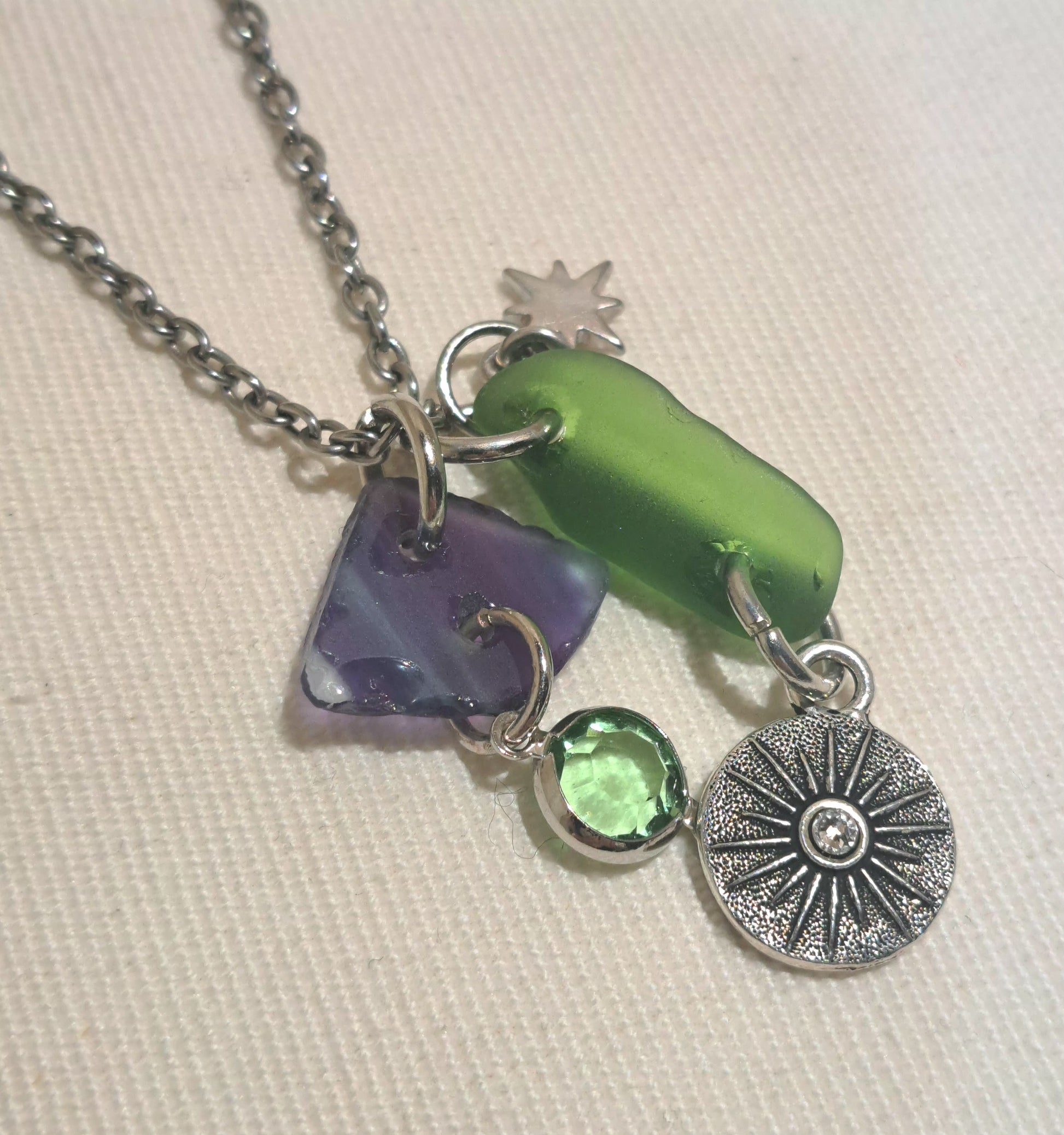 Close up of a two sea glass chips one is bright green the other in purple blue striped sea glass Includes a steel moon and sun  reversable charm