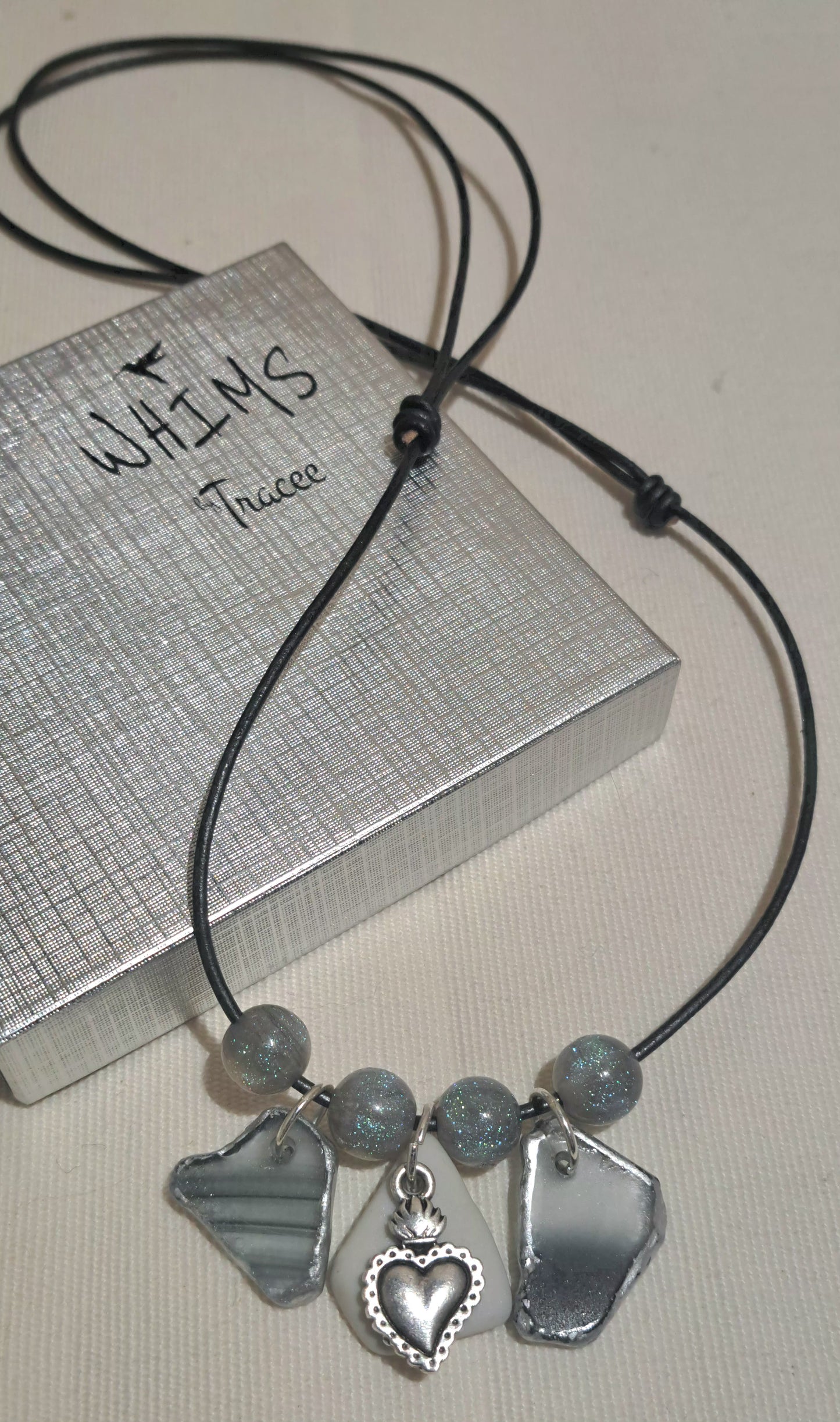 Ladies Slide knot grey leather necklace with blue resin beads and grey strped sea glass and heart charm on white tile