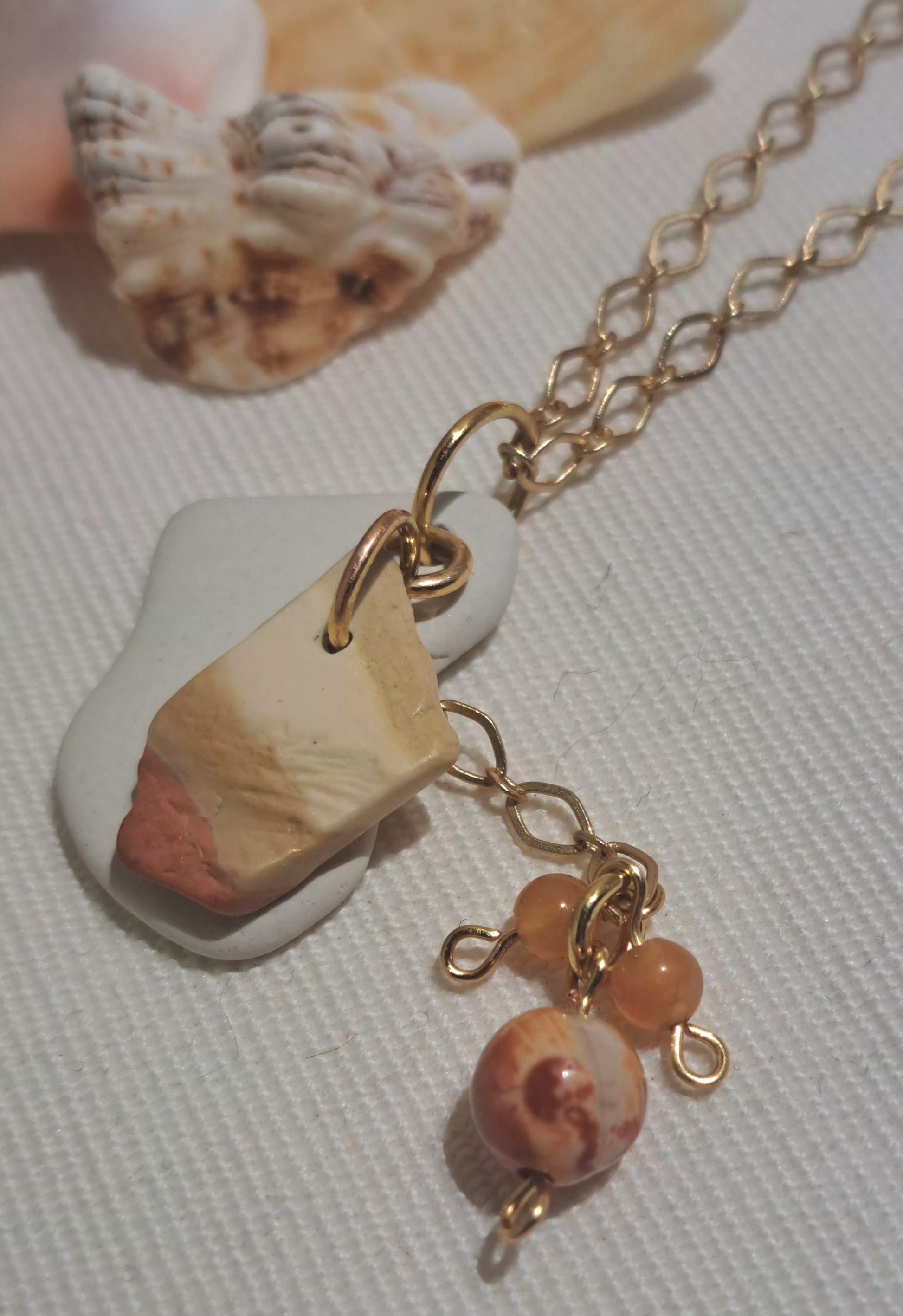 Close up of Caymanite striped stone on gold chain necklace with sea tile chip and dangling orange toned gemstone
