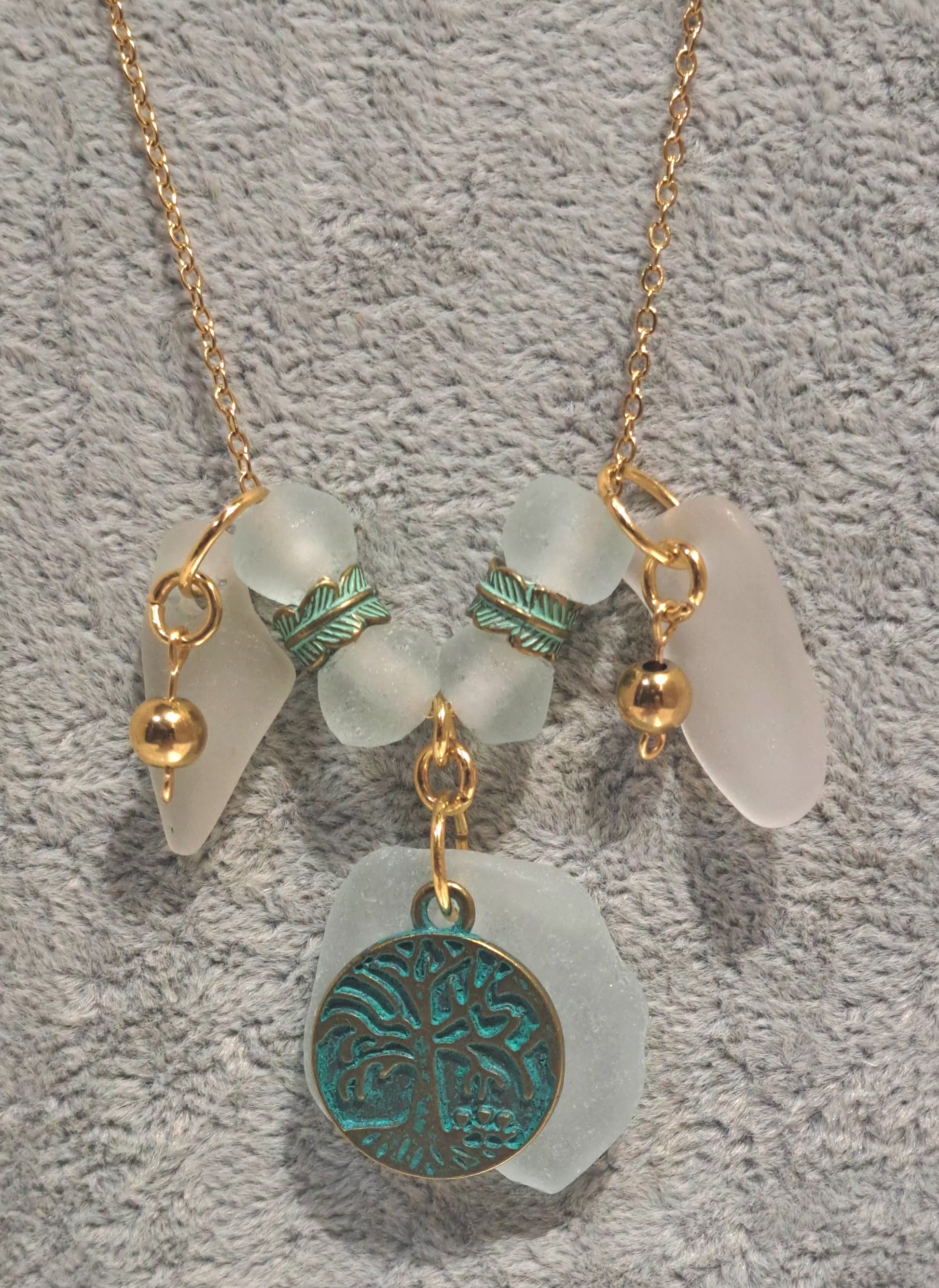 Close up view of the tree of life green brass charm necklace with accent beads and sea glass chips in pale green tones