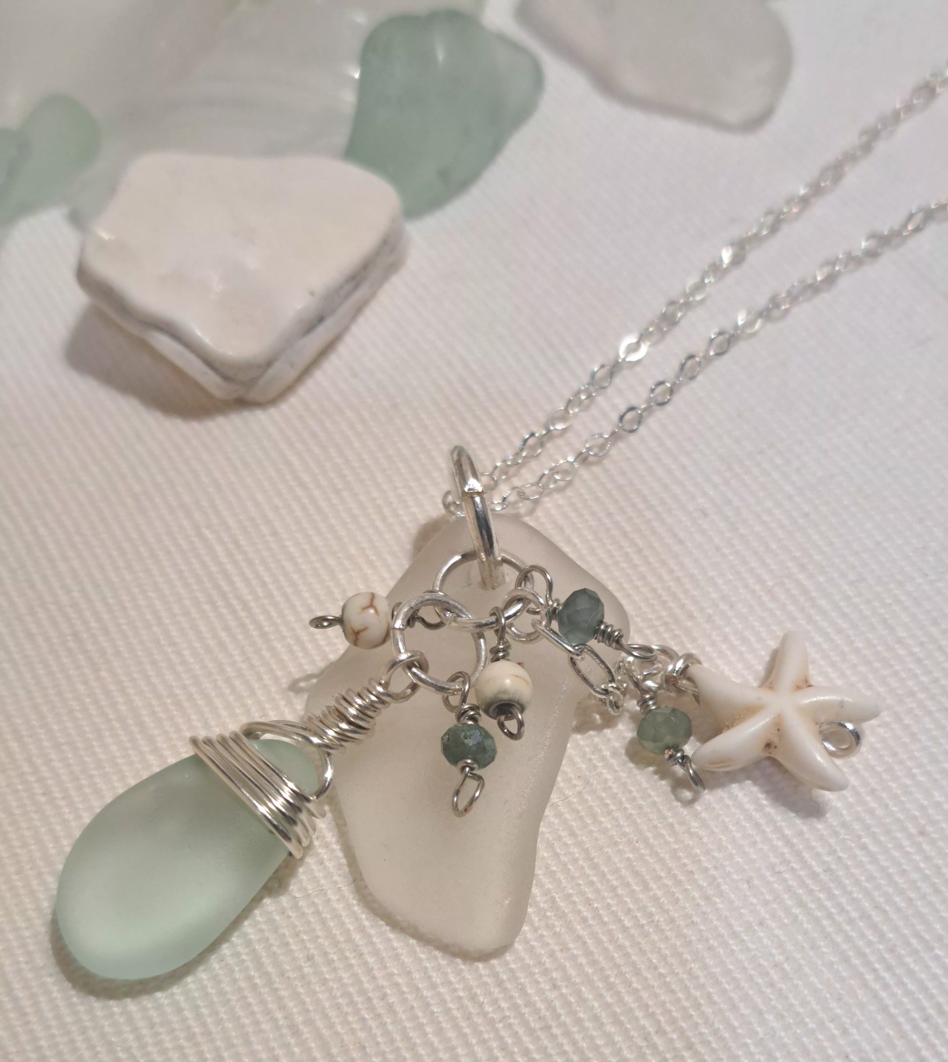 Clear sea glass chip hung on silver chain with pale green wire wrapped tear drop shaped glass and ivory star charm