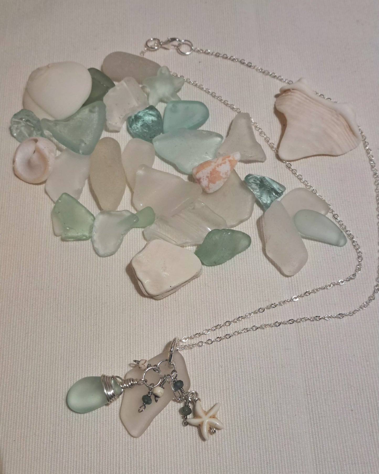 Sea glass clear and pale green with ivory star on silver chain.